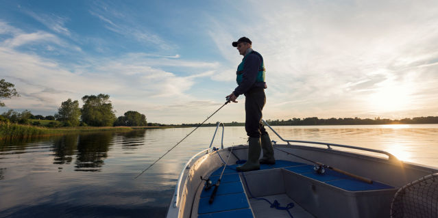 man with a hat and glasses fishing off of a small boat