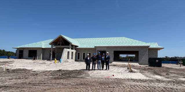 Exterior of clubhouse that is being constructed with 4 people standing in front of it