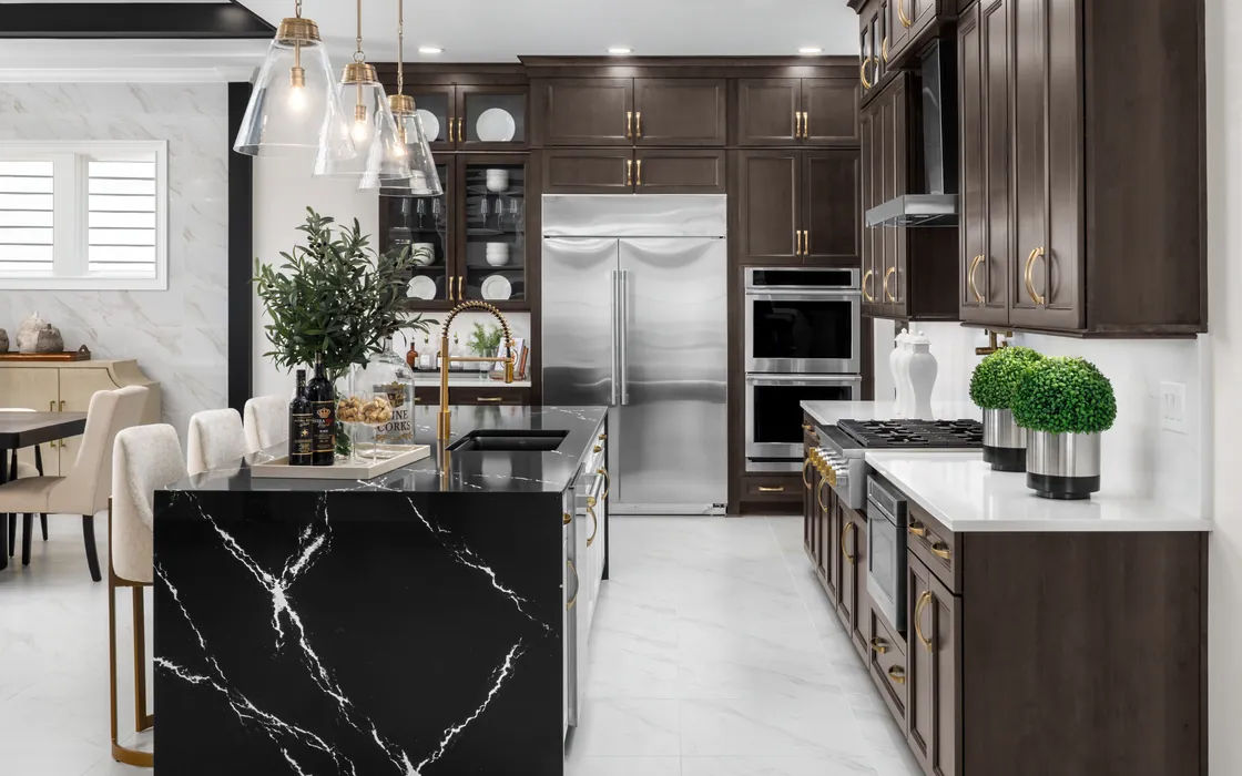 Model kitchen with a black marble waterfall island, dark wood cabinetry, brass hardware and glass pendant lights