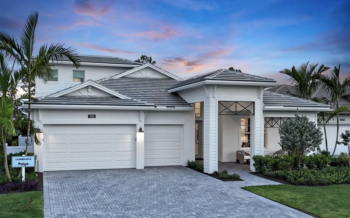 White coastal-style Kolter home at twilight with a paver driveway, palm trees and a covered entry portal
