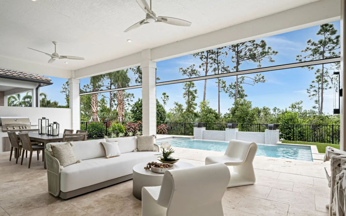 Covered lanai with white outdoor seating overlooking a private pool, water features and a pine preserve