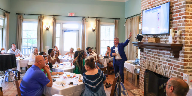 person pointing at a screen giving a presentation to a group of people that are sitting
